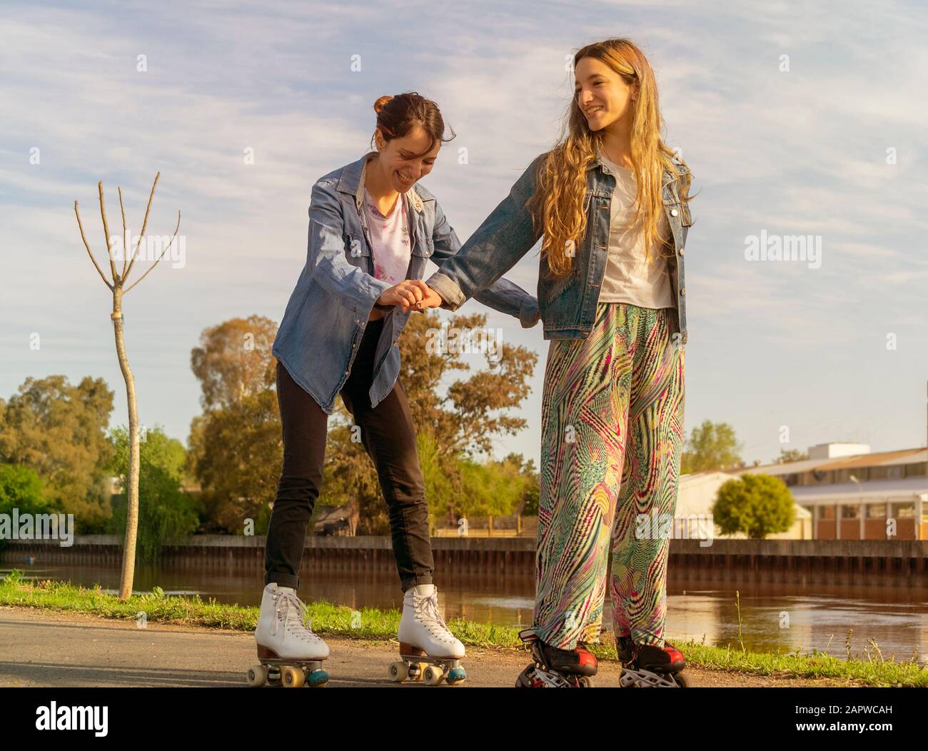 Une fille aidant à skate une autre fille tout en s'amusant, à côté de la rivière, au coucher du soleil Banque D'Images