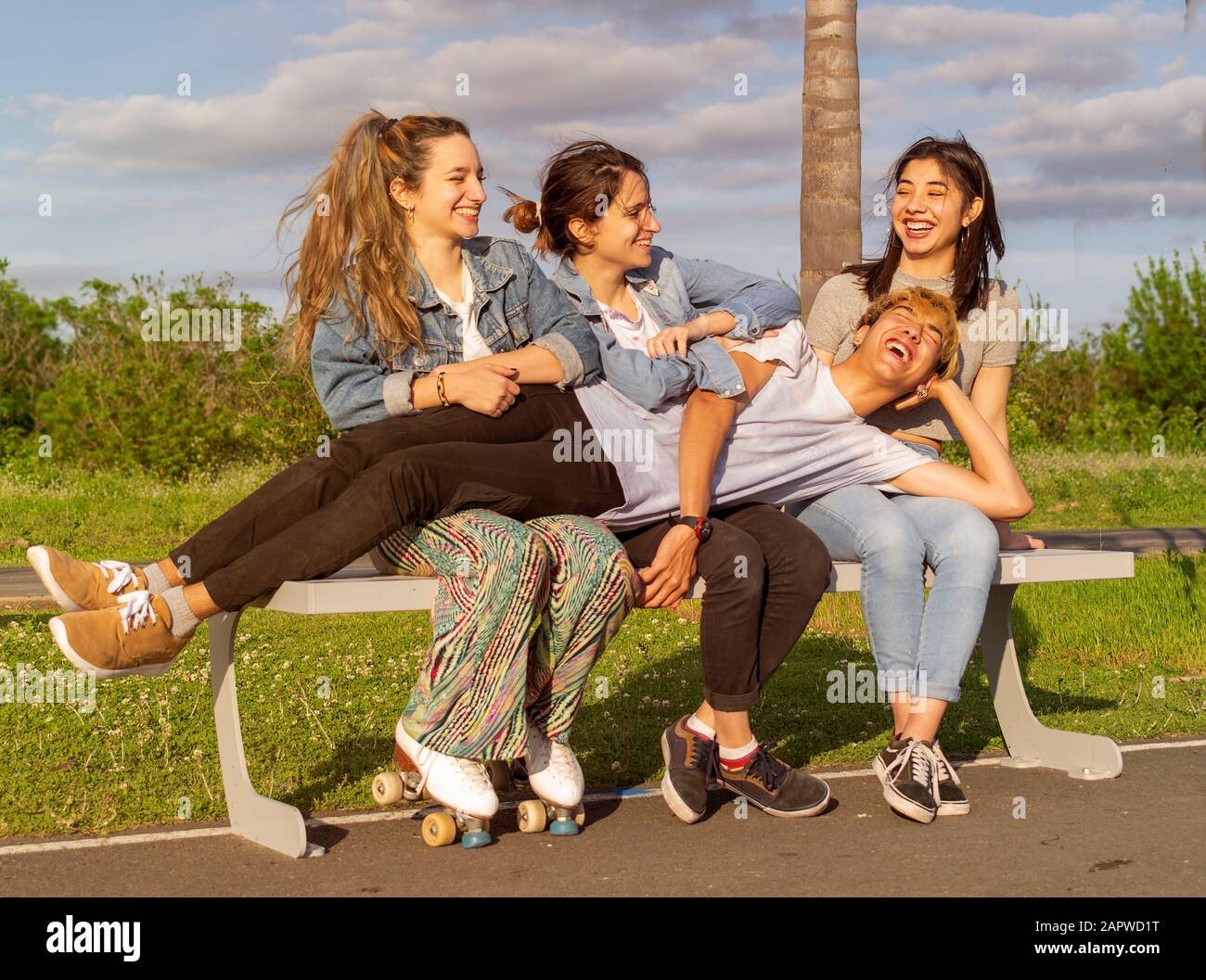 Un garçon allongé sur trois filles assis sur un banc au coucher du soleil. Tout le monde rit Banque D'Images