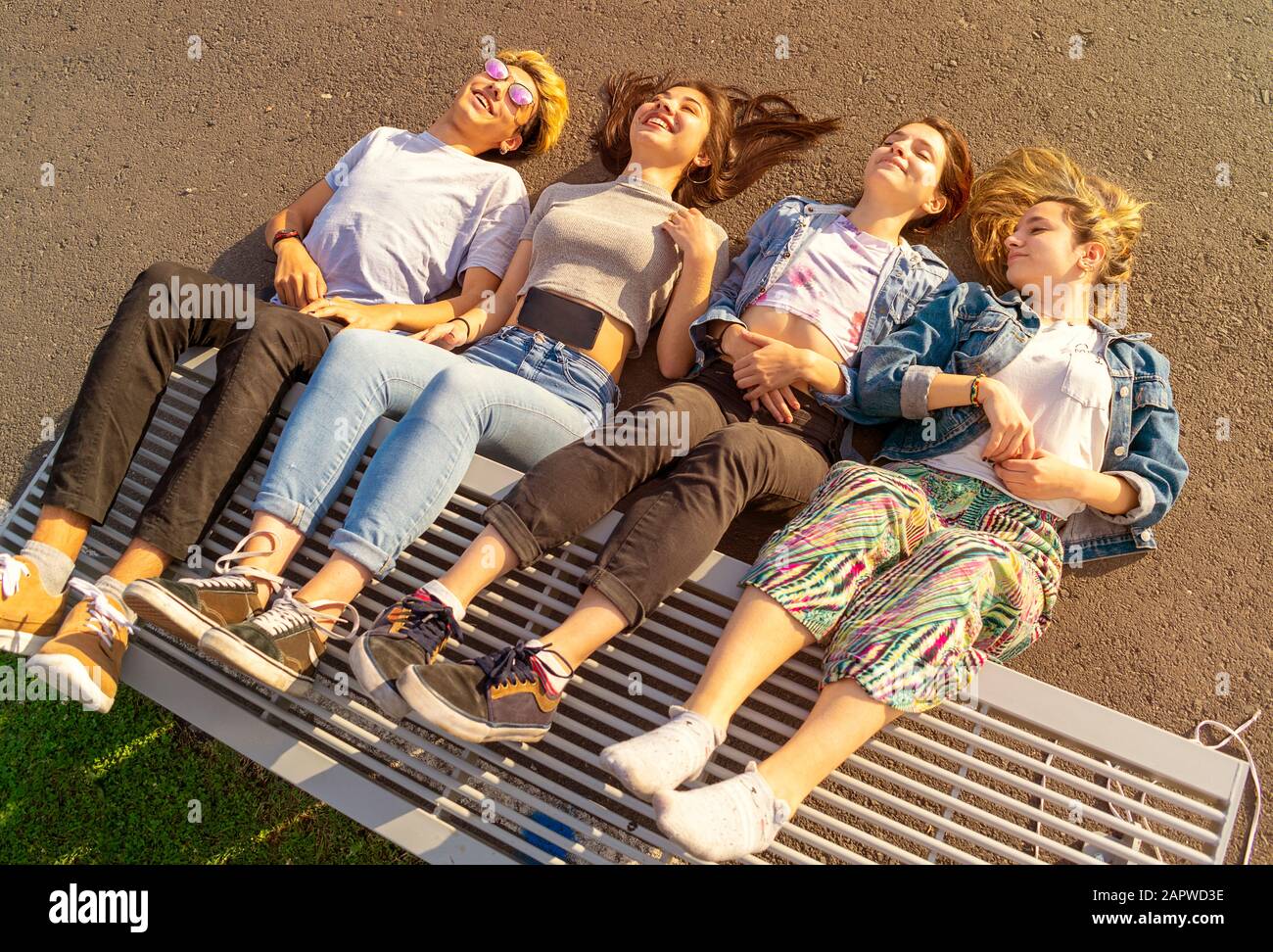 vue de dessus de quatre adolescents souriants couchant avec leurs jambes sur un banc en place au coucher du soleil Banque D'Images