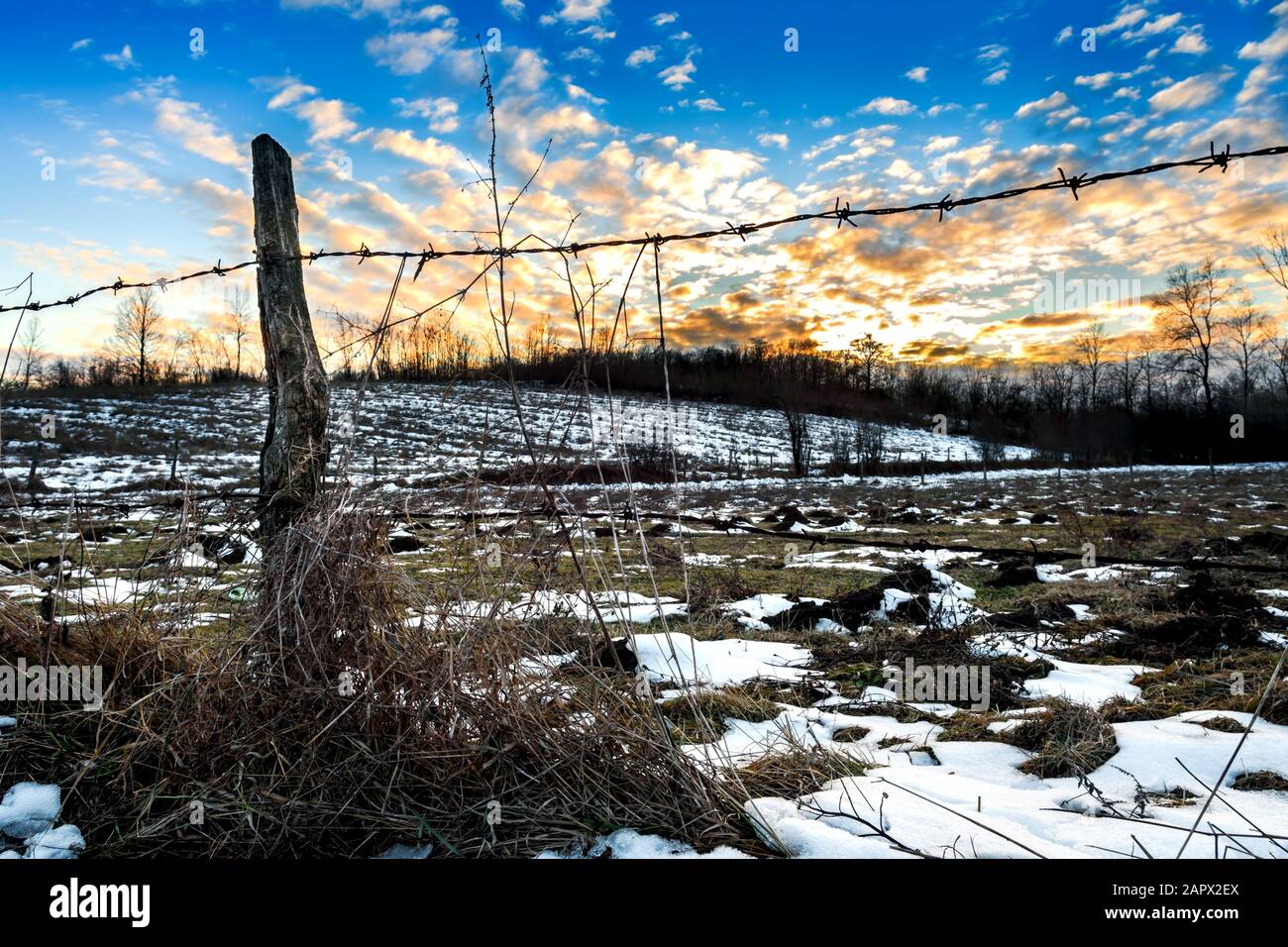 Magnifique paysage d'hiver au coucher du soleil avec clôture en fil barbelé, et ciel spectaculaire. Banque D'Images