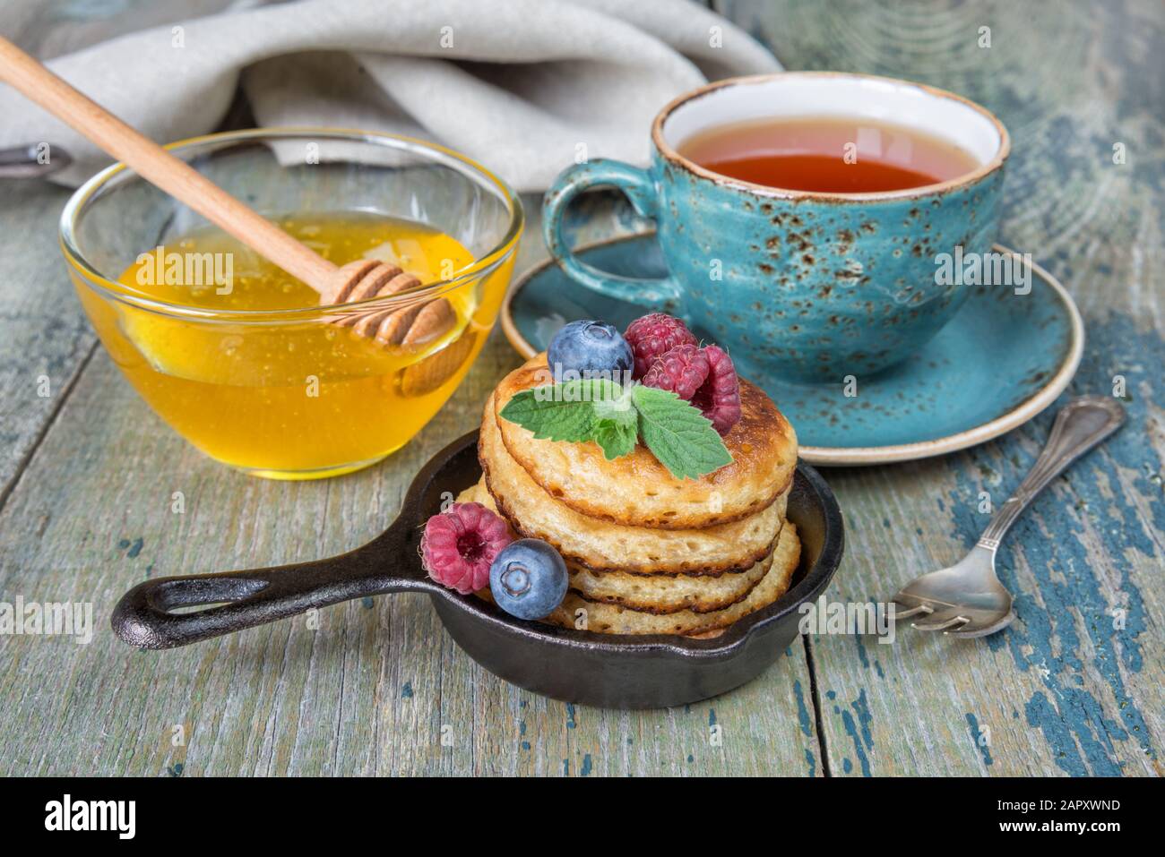 Petit-déjeuner de crêpes dans des poêles à frire en fonte, des baies fraîches, du miel et du thé noir dans un style rustique Banque D'Images