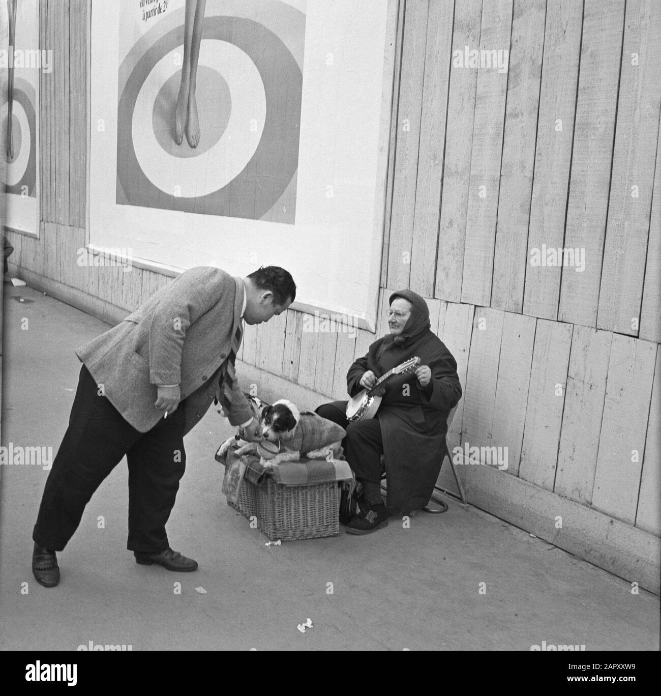 Pariser Bilder [La vie de rue de Paris] Passerby joue avec le chien d'un musicien de rue Date: 1965 lieu: France, Paris mots clés: Chiens, instruments à cordes, artistes de rue, images de rue Banque D'Images