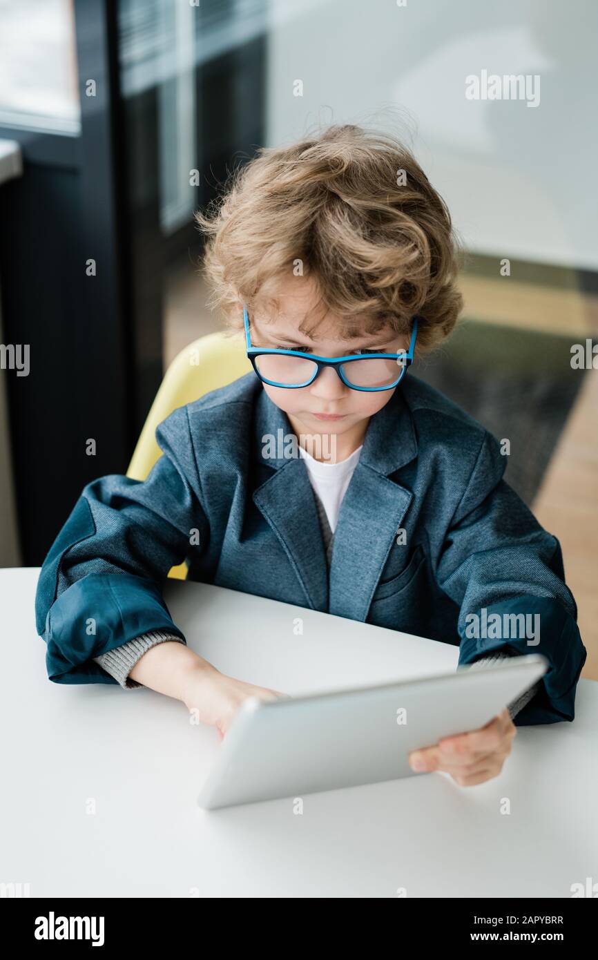 Joli garçon d'école sérieux dans des lunettes regardant l'affichage de la tablette numérique Banque D'Images