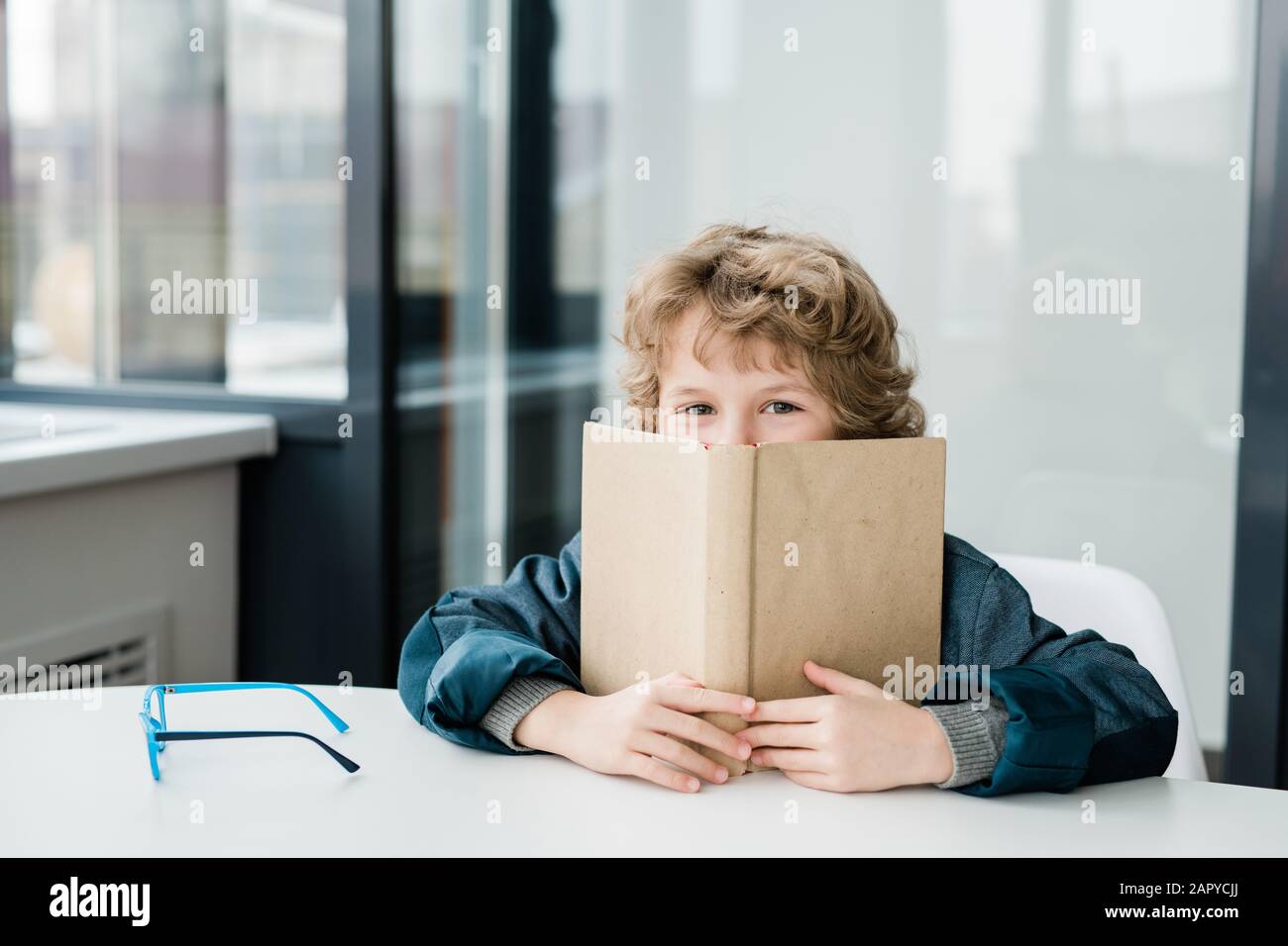 Mignon petit garçon d'école peeking hors du livre ouvert à la leçon de la littérature Banque D'Images