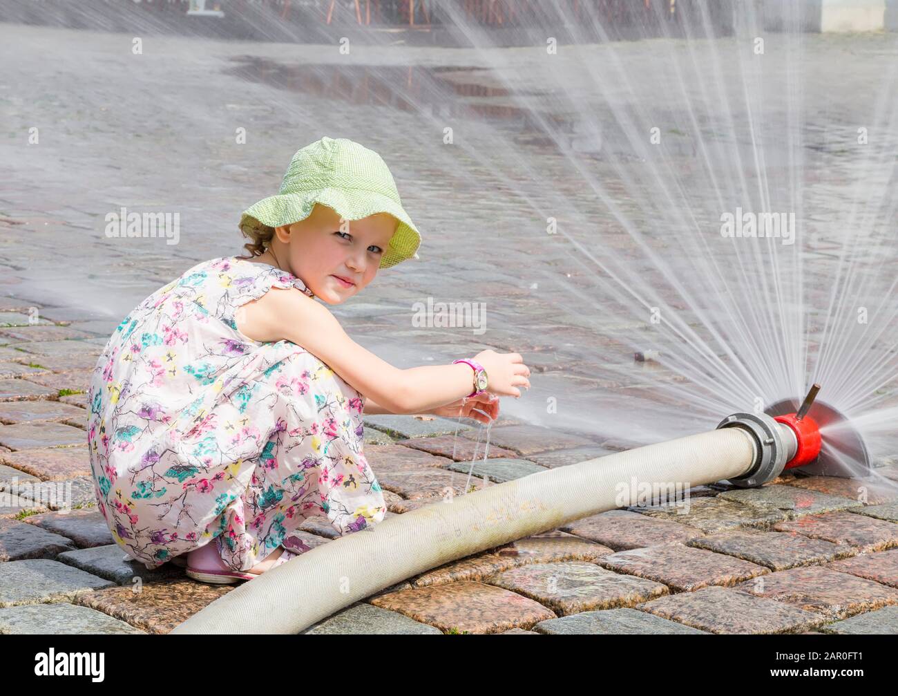 Une petite fille joue avec un jet d'eau à partir d'un tuyau sur une chaude journée d'été Banque D'Images