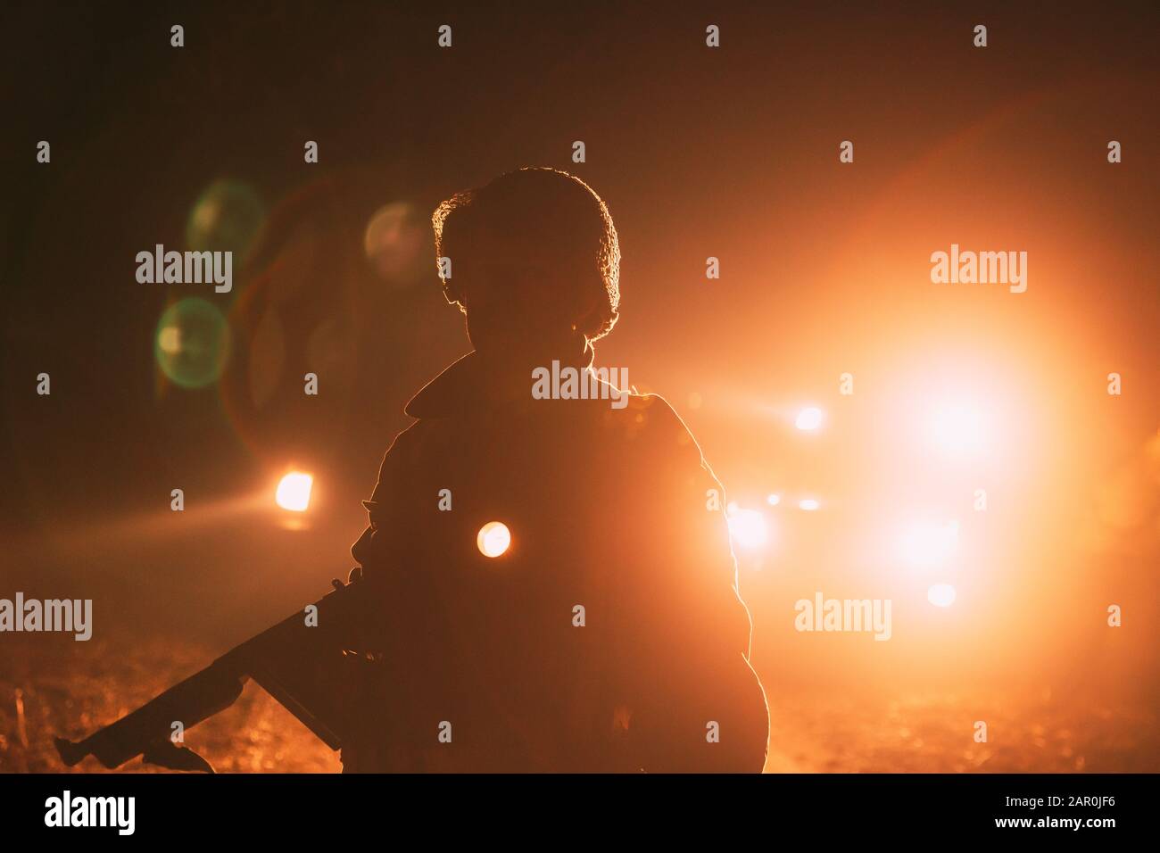 Réacteur Vêtu Comme Soldat De L'Infantry Of World War Ii Des Etats-Unis, Il Tient L'Arme De Sous-Machine Entre Les Mains. Portrait En Touche Bas. Lumière Des Véhicules Automobiles Feux Banque D'Images