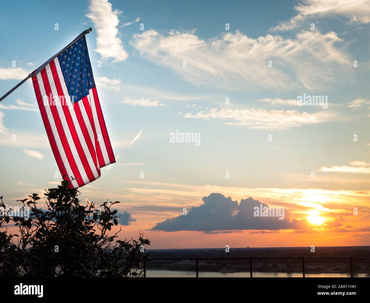 Drapeau américain brillant volant au-dessus du magnifique coucher de soleil sur le fleuve Mississippi. Symbole du patriotisme et de la paix. L'arrière-plan affiche les nuages éclairés i Banque D'Images
