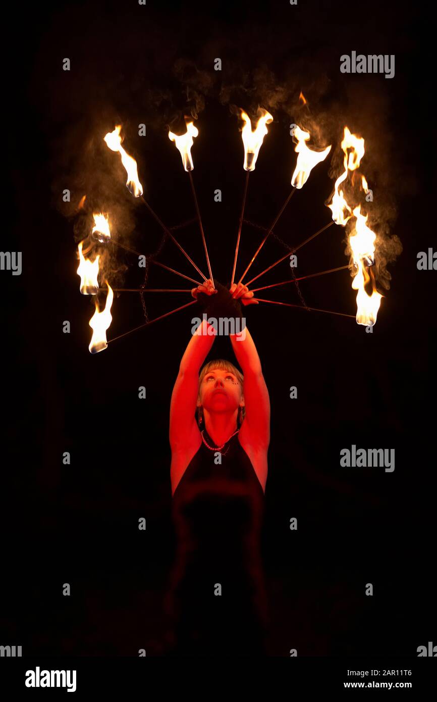 femme artiste de feu tenant des ventilateurs de feu allumés au-dessus de sa tête la nuit pendant le spectacle Banque D'Images