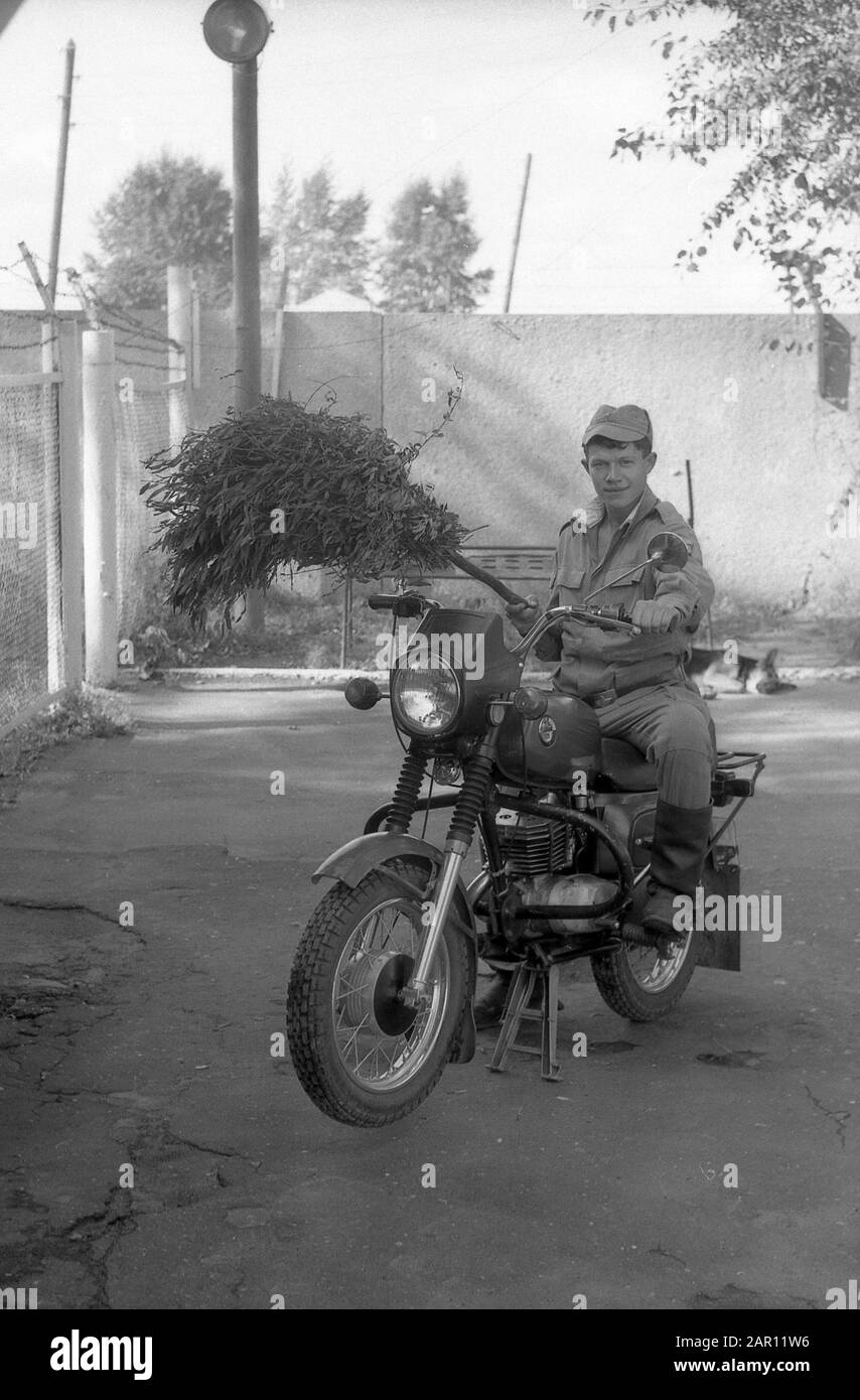 STUPINO, RÉGION DE MOSCOU, RUSSIE - VERS 1993: Portrait d'un officier de l'armée russe sur une moto et un balai dans sa main. Noir et blanc. Numérisation de film. Gros grain. Banque D'Images