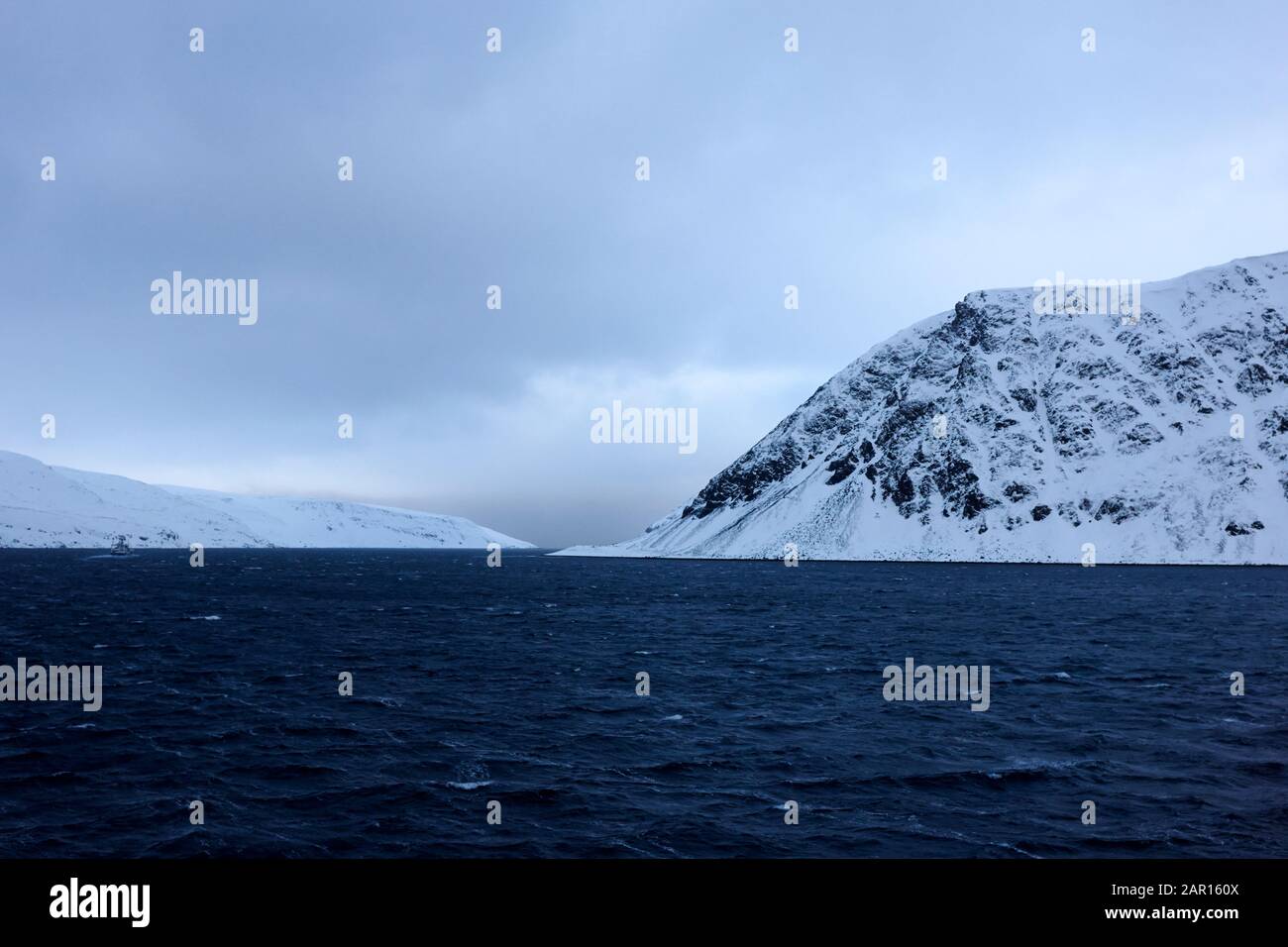 naviguer dans la neige couvrait les fjords norvégiens avec un petit bateau de pêche dans la distance finnmark norvège Banque D'Images