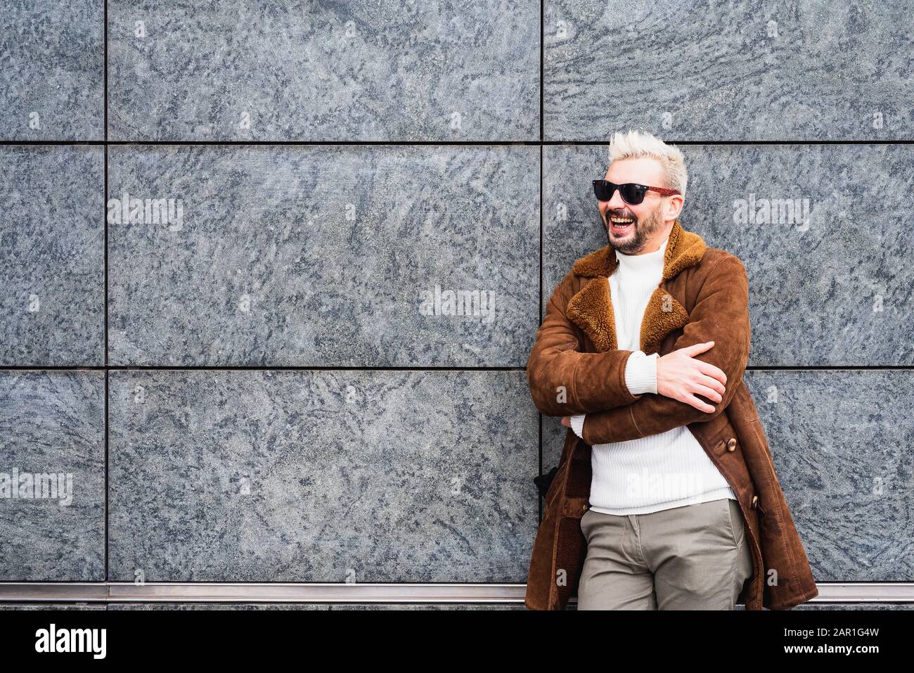 L'homme gai est debout avec ses bras repliés et il sourit heureux, l'homme barbu avec des lunettes de soleil rit Banque D'Images