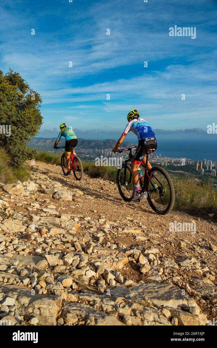 Deux cyclistes de montagne en montagne sur la colline avec Benidorm ville en arrière-plan, Sierra Cortina, Benidorm, province d'Alicante, Espagne Banque D'Images