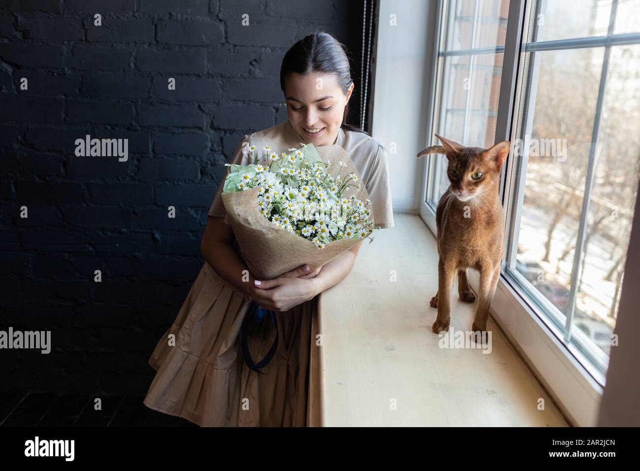 Fille dans une robe avec un chat bengal et bouqet de fleurs près de la  fenêtre en face de l'appareil photo Photo Stock - Alamy
