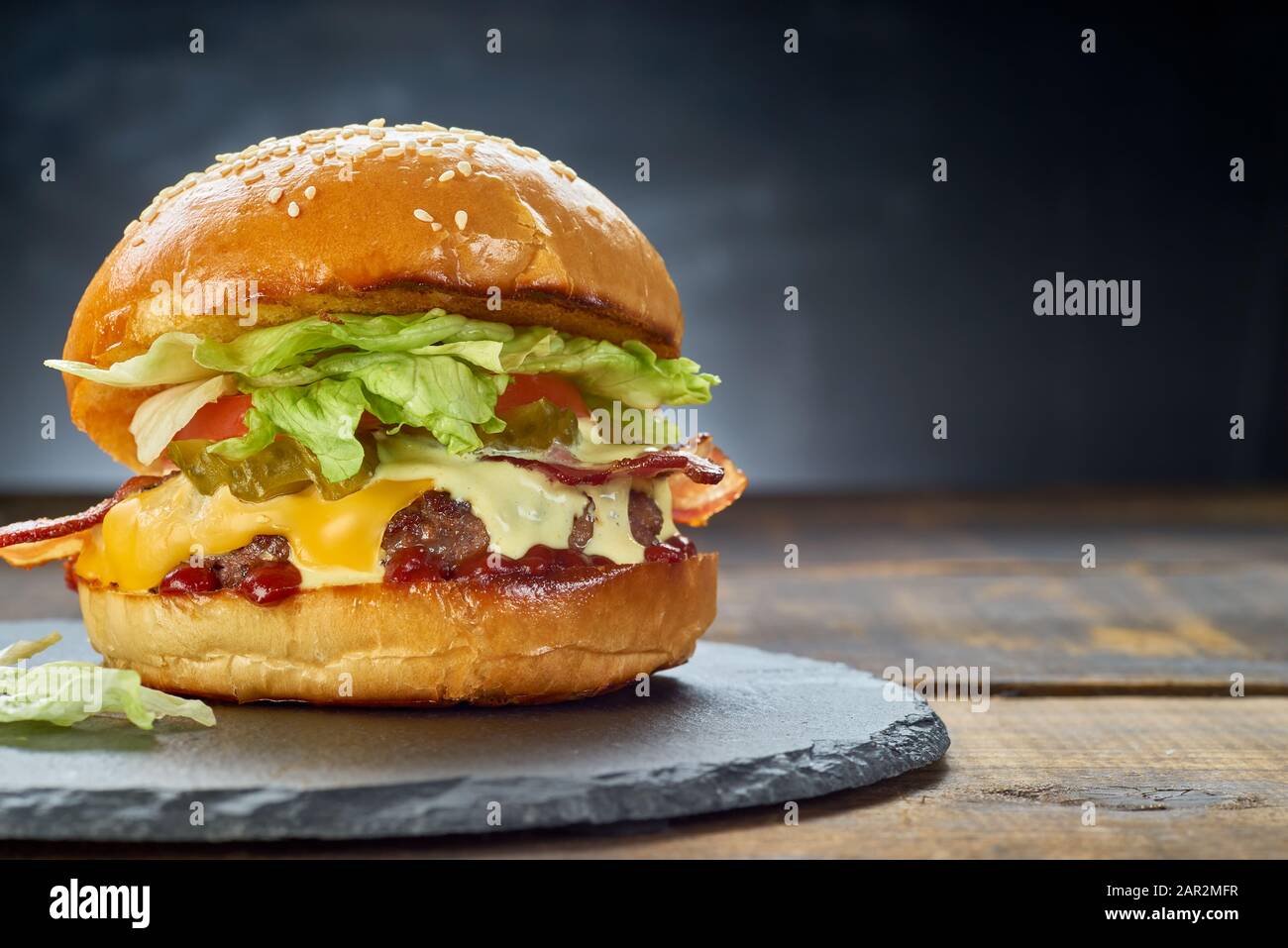 Gros hamburger sur un plat noir en ardoise sur fond sombre. Espace de copie Banque D'Images