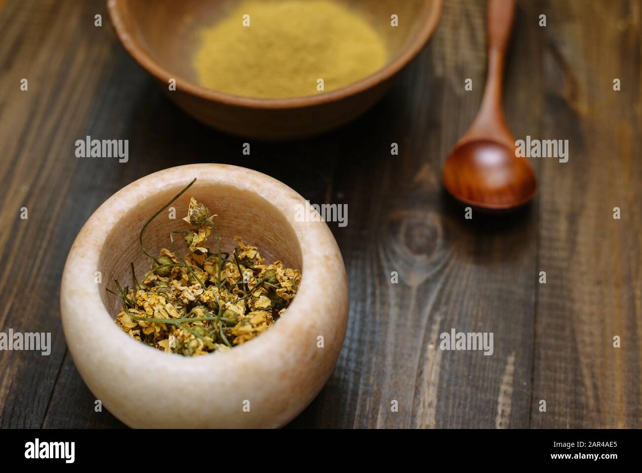 Mortier de marbre avec camomille séchée pour cosmétiques naturels. Bol en argile avec poudre jaune ou argile et fleurs sur fond en bois. Pose plate. Banque D'Images