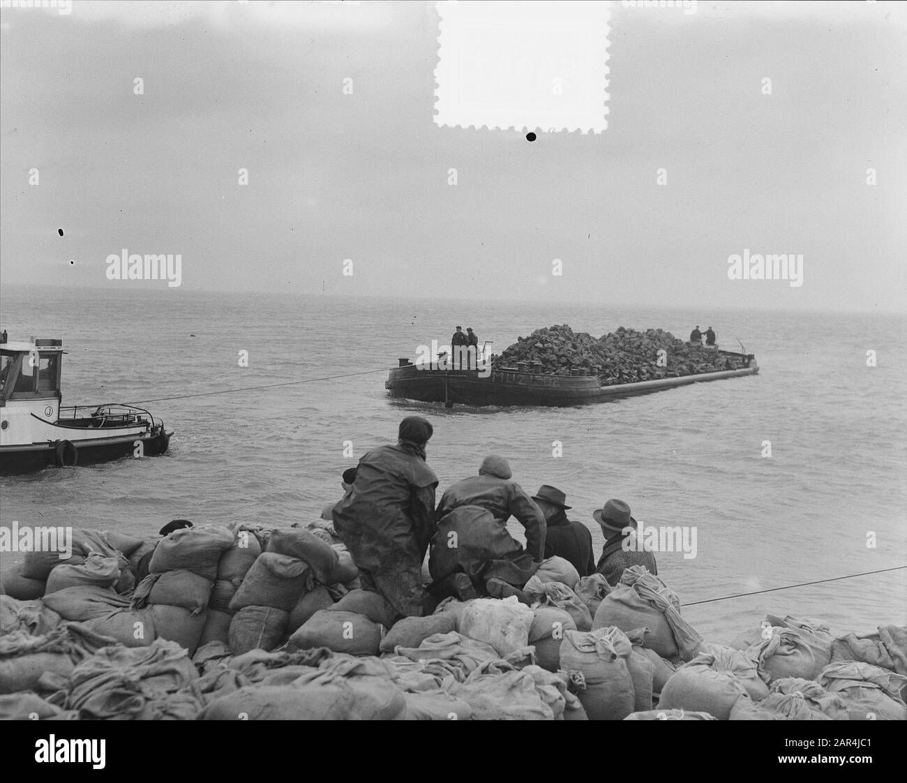 Watersnood 1953] le trou de digue près de Herkingen op Goeree-Overflakkee, qui a été fait au début de février 1953, mais qui n'a pas été fermé à temps, est maintenant fermé avec des blocs de basalte. Les barges de grenier avec ces blocs sont navigué dans le trou, et à grande vitesse les morceaux de basalte sont ensuite jetés dans l'eau. Date : 12 Mars 1953 Lieu : Goeree-Overflakkee, Herkingen, Zuid-Holland Mots Clés : Restaurations, Inondations Banque D'Images
