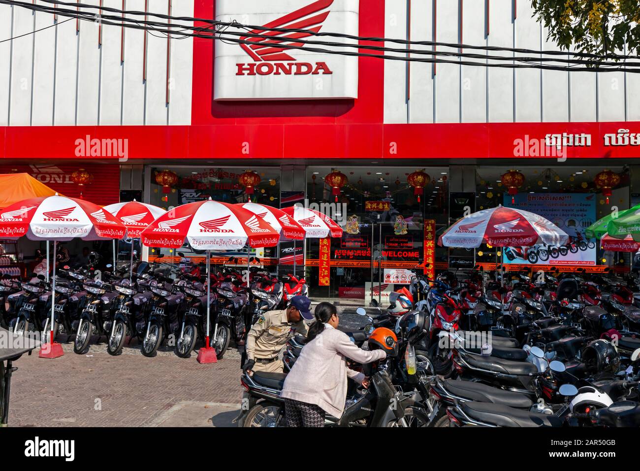 Policier son aide à une femme à déplacer sa moto Honda devant une concession de moto Honda à Phnom Penh, au Cambodge Banque D'Images Policier son aide à une femme à déplacer sa moto Honda devant une concession de moto Honda à Phnom Penh, au Cambodge Banque D'Images