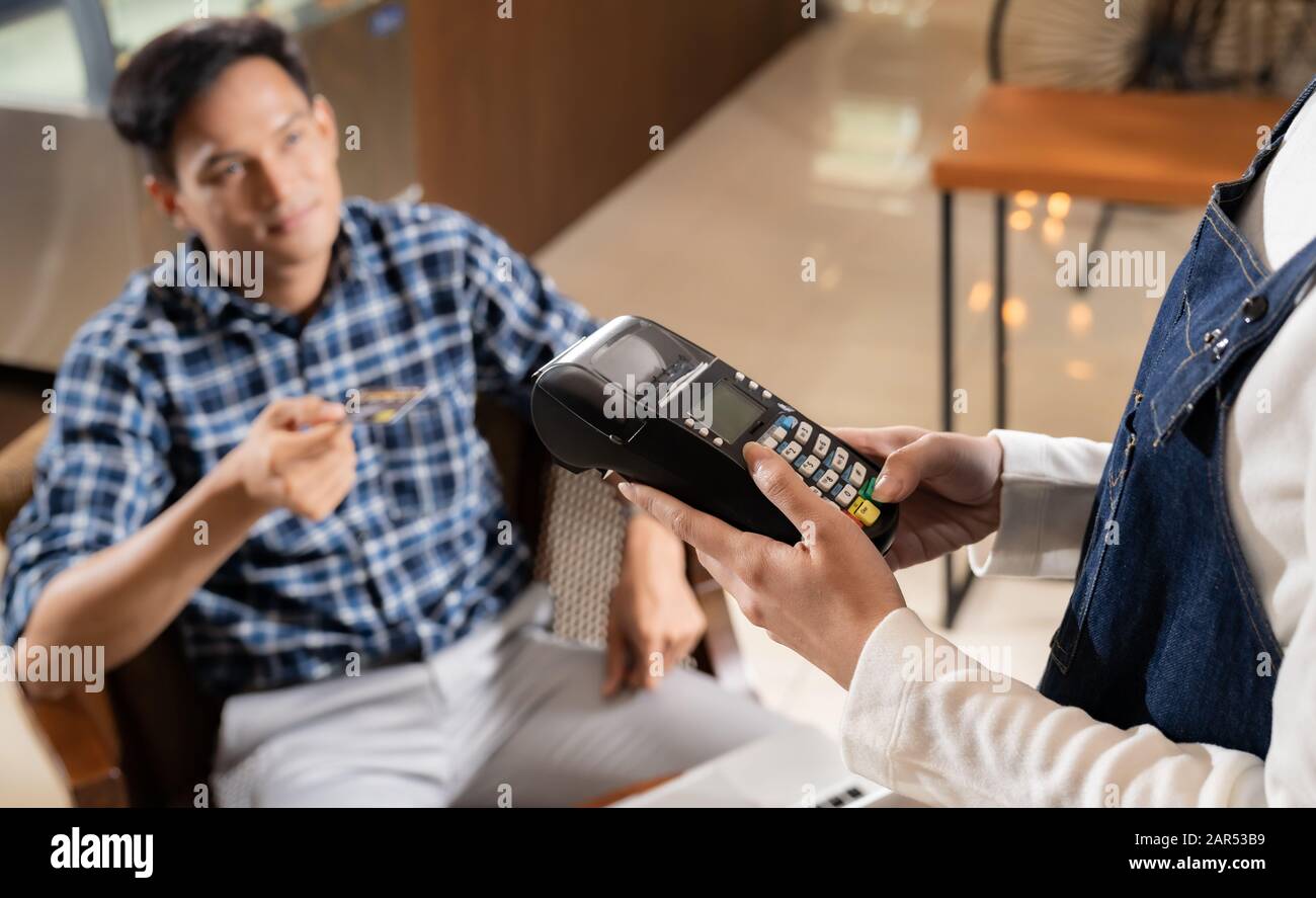 Client asiatique utilisant une carte de crédit avec la technologie de puce EMV pour payer une serveuse pour l'achat de café à la table dans le café. Banque D'Images