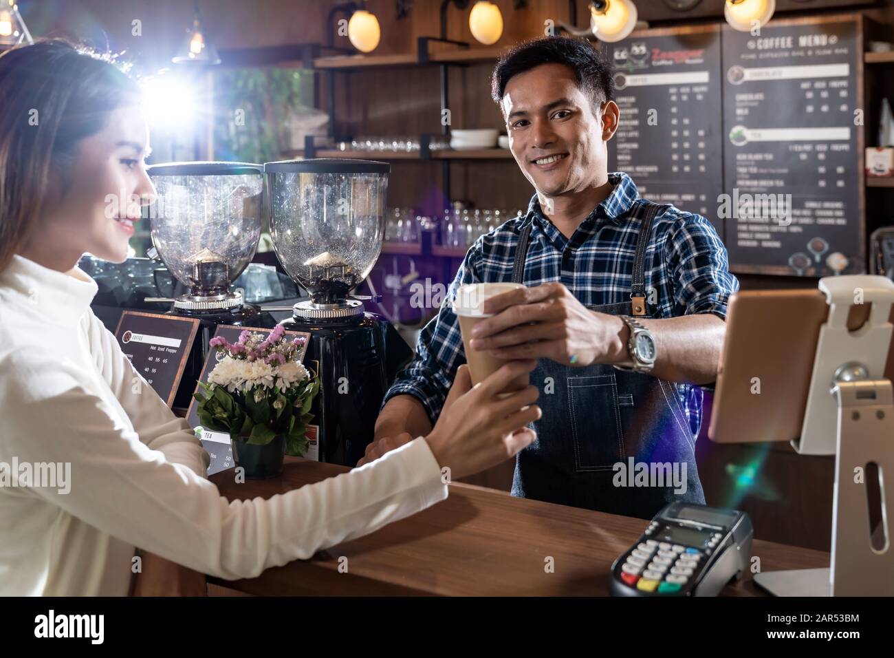 Portrait du barista asiatique tient une tasse de café à emporter et sert au client dans un café. Banque D'Images