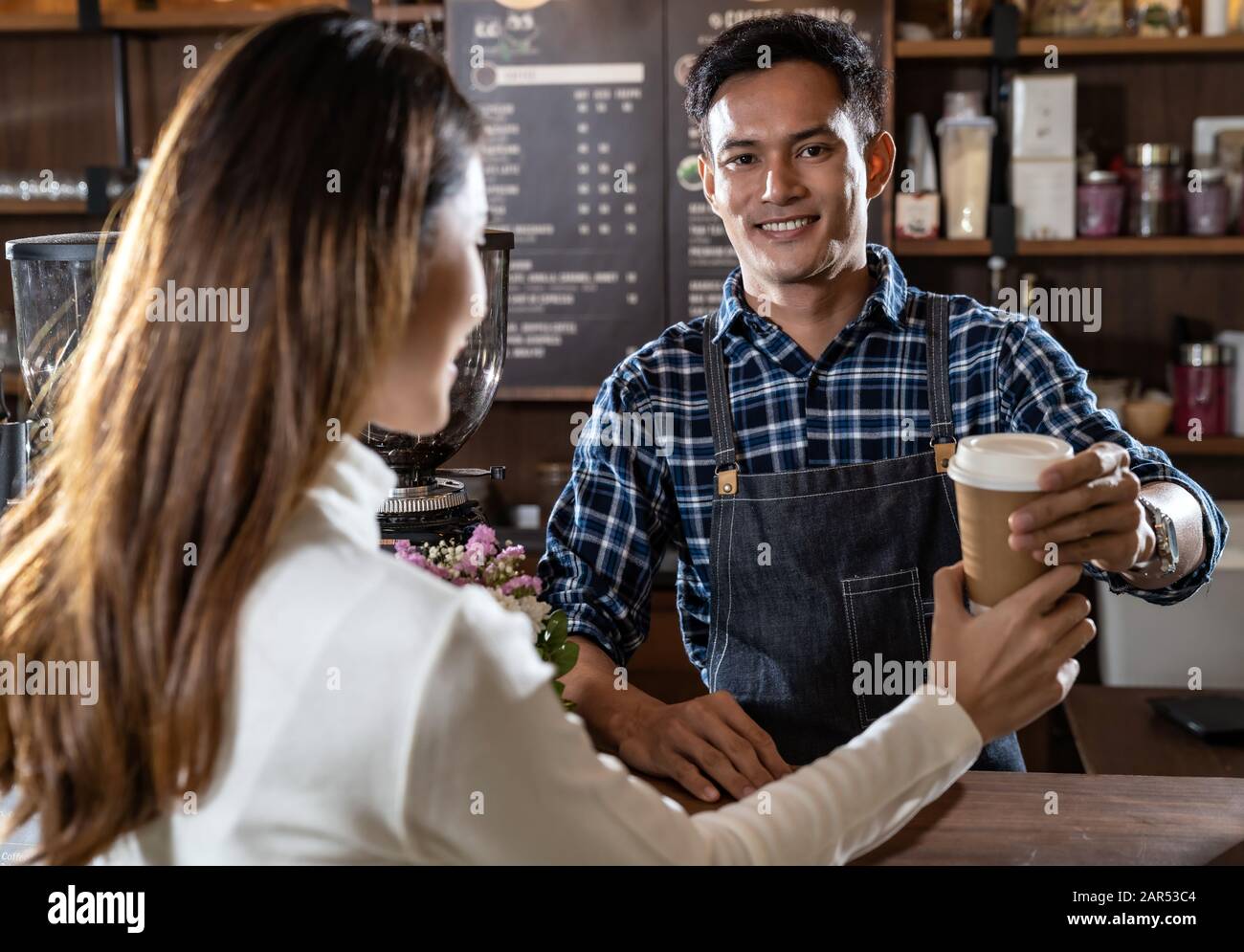 Portrait du barista asiatique tient une tasse de café à emporter et sert au client dans un café. Banque D'Images