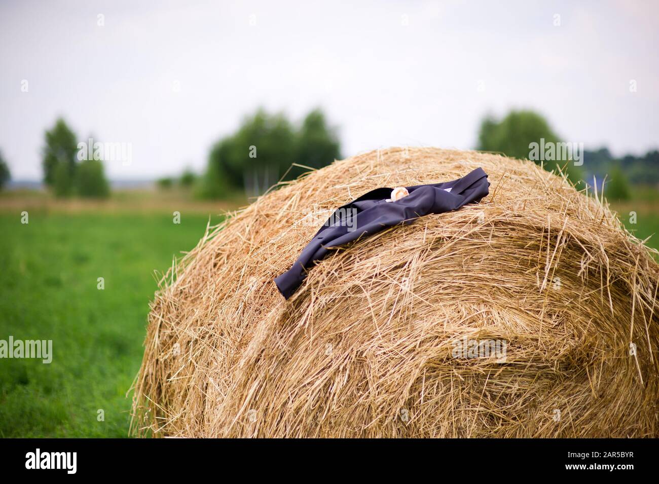 Une veste d'homme avec une boutonnière se trouve sur une haystack lors d'une journée d'été nuageux dans le village. Gros plan Banque D'Images