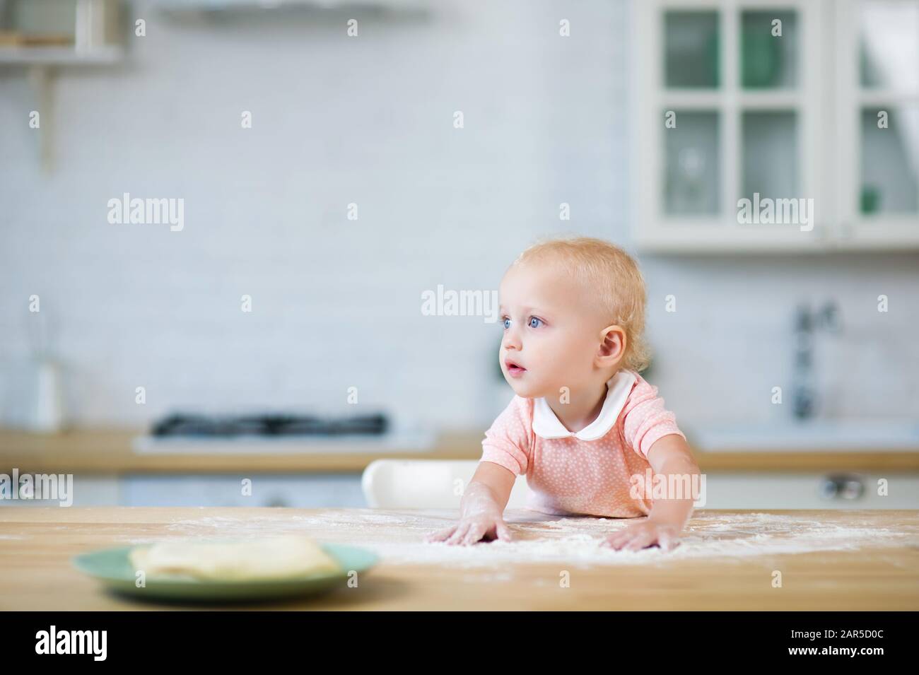 une fillette blonde aux yeux bleus mène ses mains sur le comptoir avec de la farine et regarde loin Banque D'Images