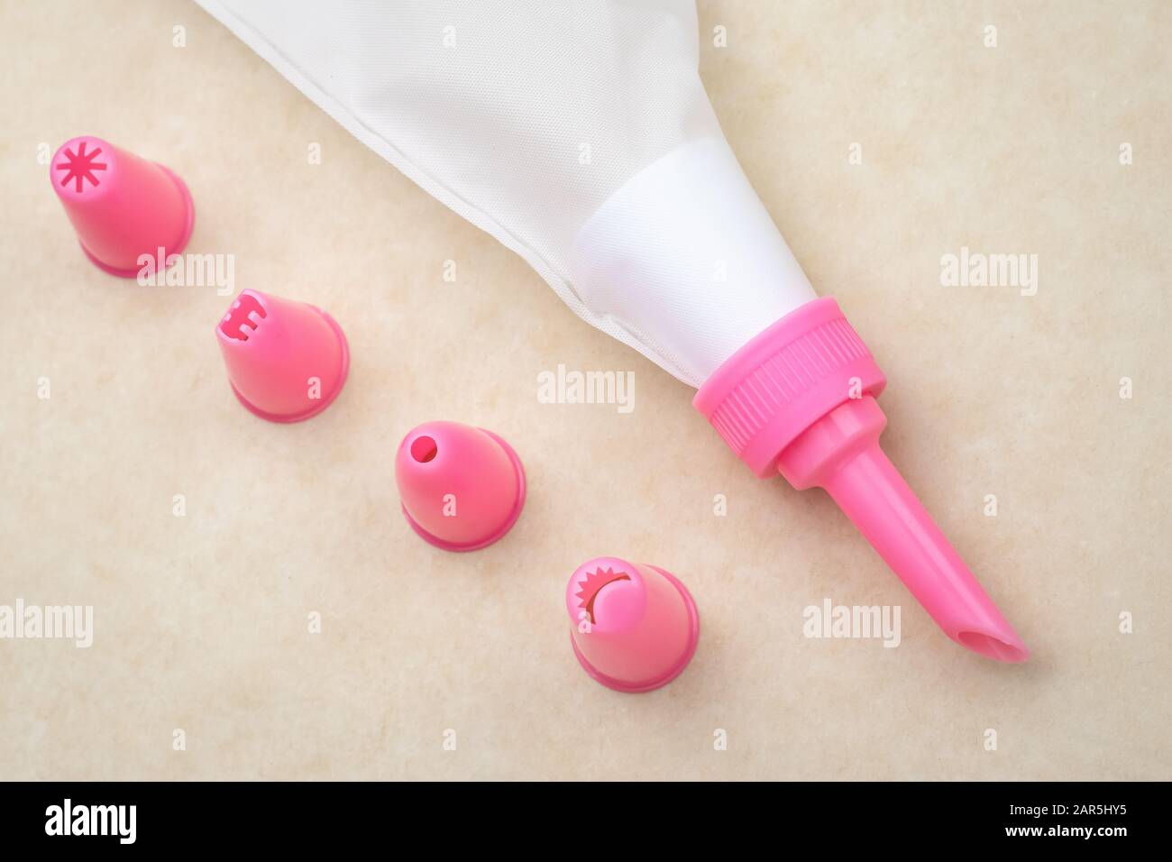 Le sac à pâtisserie avec des buses roses sur fond de papier neutre pour la décoration des gâteaux Banque D'Images