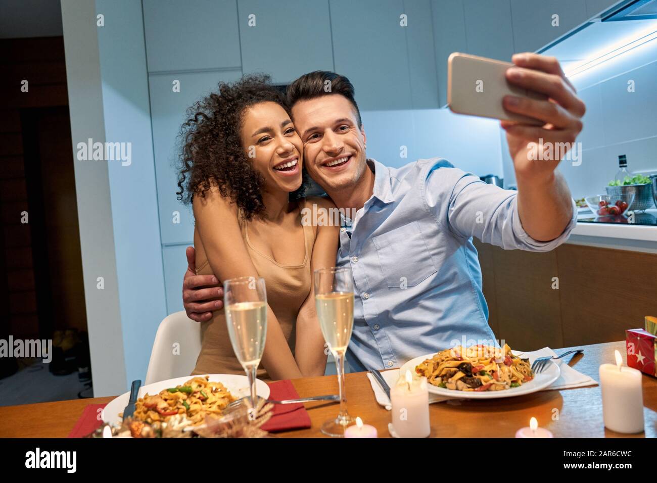 Date Romantique. Jeune couple multiethnique à la maison après avoir dîné embrassant prendre selfie sur smartphone pour sauver des moments de rire gai Banque D'Images