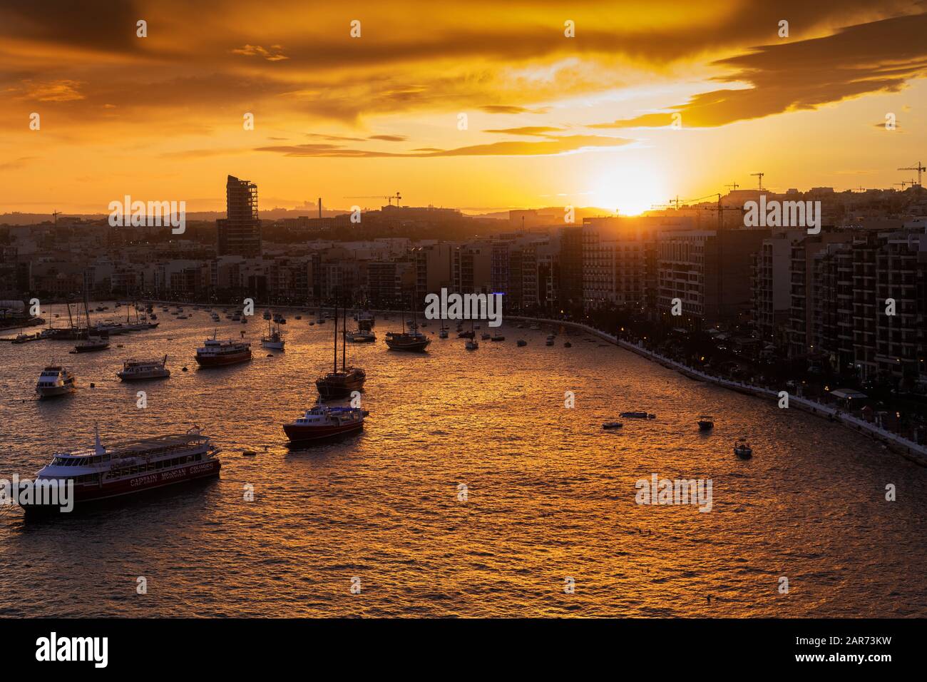 Coucher de soleil au-dessus de la ville de Sliema à Malte, bateaux et lumière du soleil reflétés dans le port de Marsamxett Banque D'Images