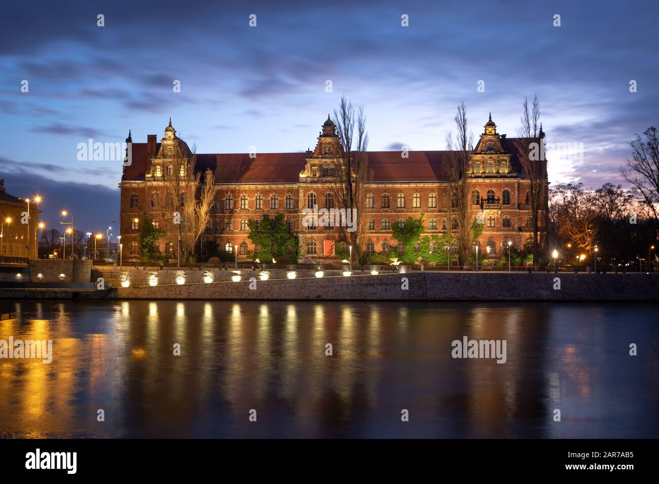 Wroclaw, Pologne. Bâtiment historique lumineux du Musée national reflétant dans la rivière Oder au crépuscule Banque D'Images