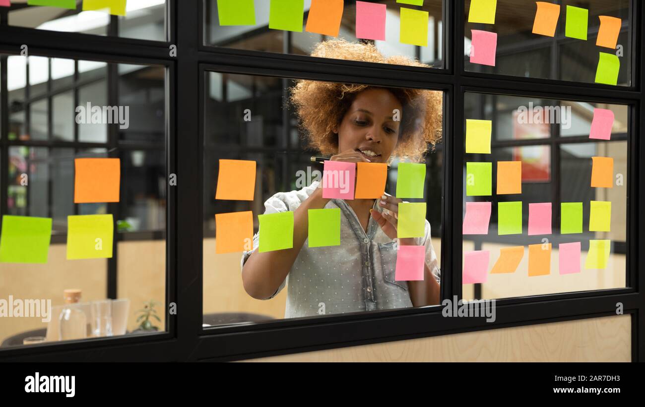 L'employé féminin afro-américain élabore un plan sur les notes collantes Banque D'Images