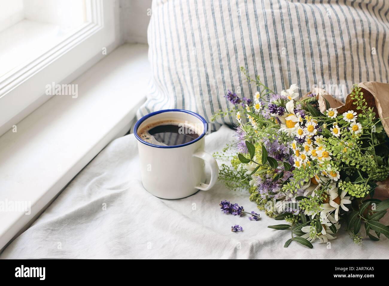 Scène de petit-déjeuner d'été. Mug en émail, bouquet de fleurs sauvages et coussin en lin. Photo féminine vintage, design rustique, composition florale avec café, vbl Banque D'Images