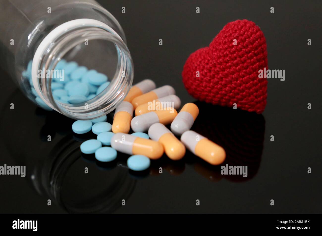 Pilules et coeur rouge tricoté sur table en verre foncé, bouteille avec médicament en capsules. Concept d'hypertension, de maladie cardiaque, de cardiologie, d'examen préliminaire sanguin Banque D'Images