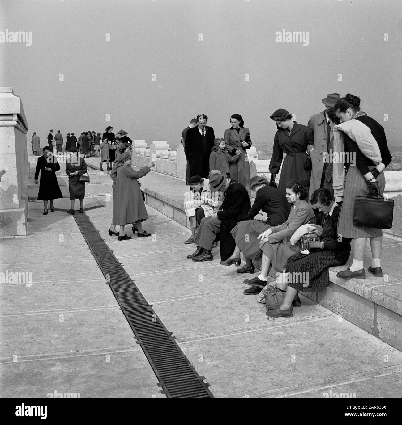 Années 1950, historique, printanière et visiteurs dans les modes de la journée, assis et debout sur le toit en pierre d'un grand bâtiment à Paris, France. Banque D'Images