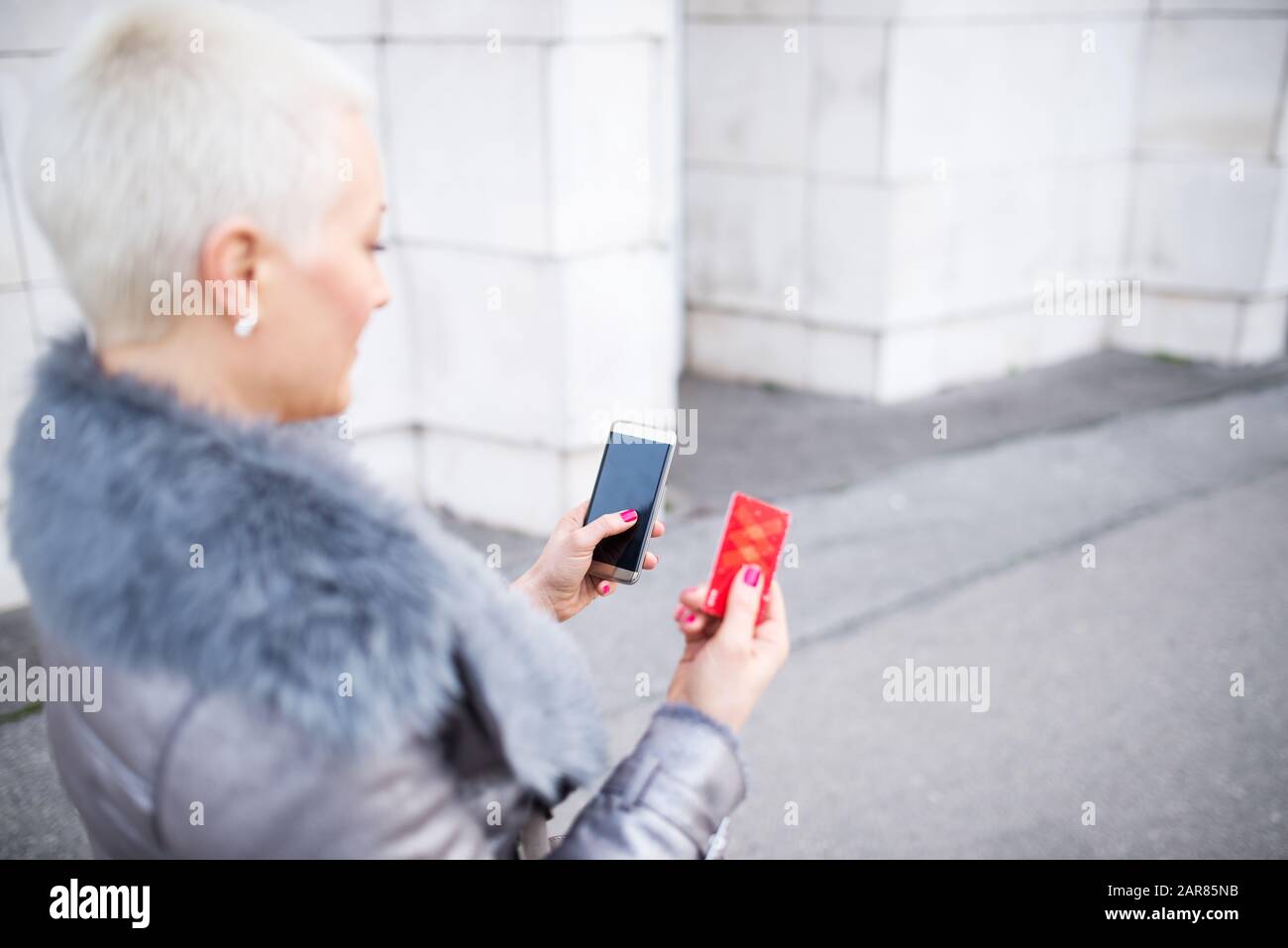 La femme dans la rue utilise un téléphone portable et tient une carte de paiement Banque D'Images