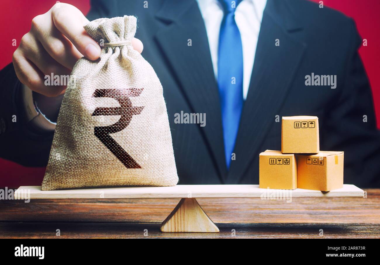 Homme d'affaires met le sac d'argent de roupie indienne et des tas de boîtes sur les balances. Balance des échanges commerciaux. Importation et exportation, processus économiques. Bénéfice du fabricant Banque D'Images