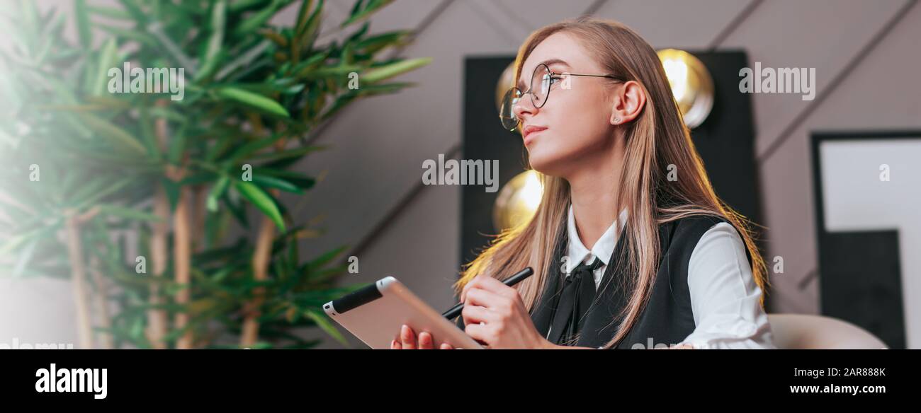 Beauté jeune femme en lunettes assis dans le bureau avec une tablette, générant des idées. Plantes en arrière-plan. Affaires et éducation Banque D'Images