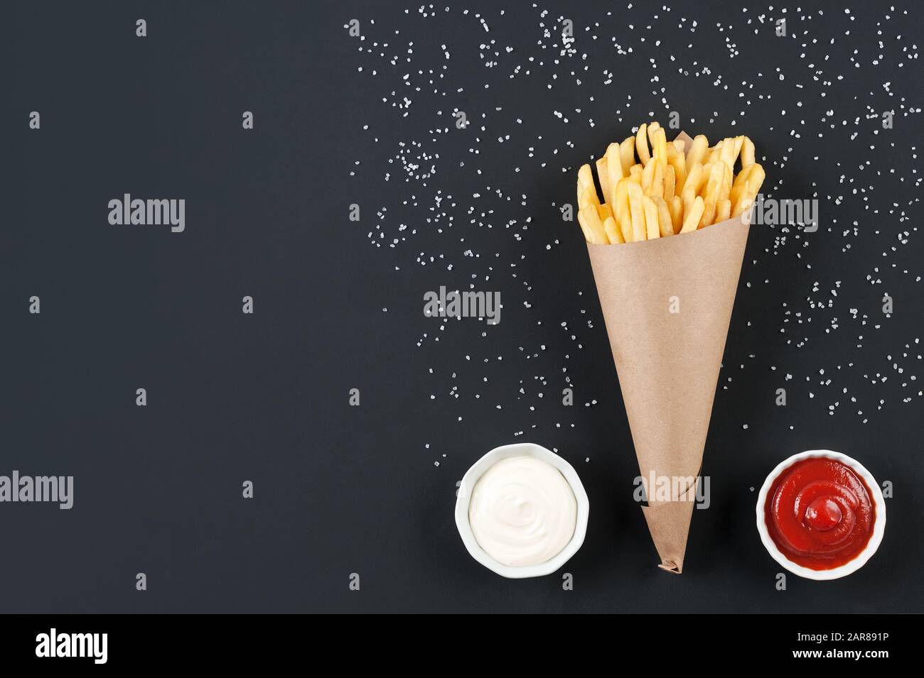 Frites savoureuses de pommes de terre avec sauces ketchup et mayonnaise sur fond noir. Frites dans le cône en papier. Banque D'Images