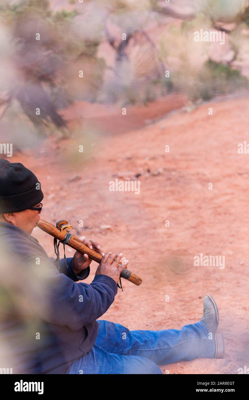 Navajo homme adulte est assis dans le sable jouant une flûte Navajo à Mystery Valley, Monument Valley Tribal Park, Arizona, États-Unis Banque D'Images