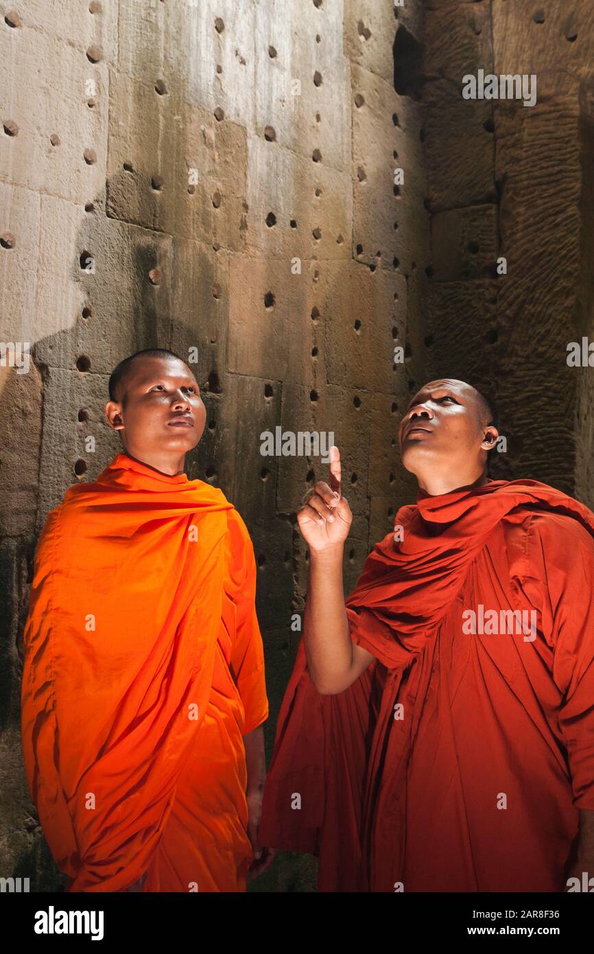 Deux moines mâles en robes orange se trouvent dans une niche aux ruines d'Angkor Wat, Siem Reap, Cambodge Banque D'Images