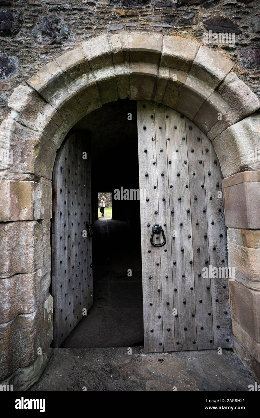 La vue lointaine d'une touriste féminine à travers la porte voûtée a une porte en bois usée massive entourée de briques en pierre, le château de Dunstaffnage datant de t Banque D'Images