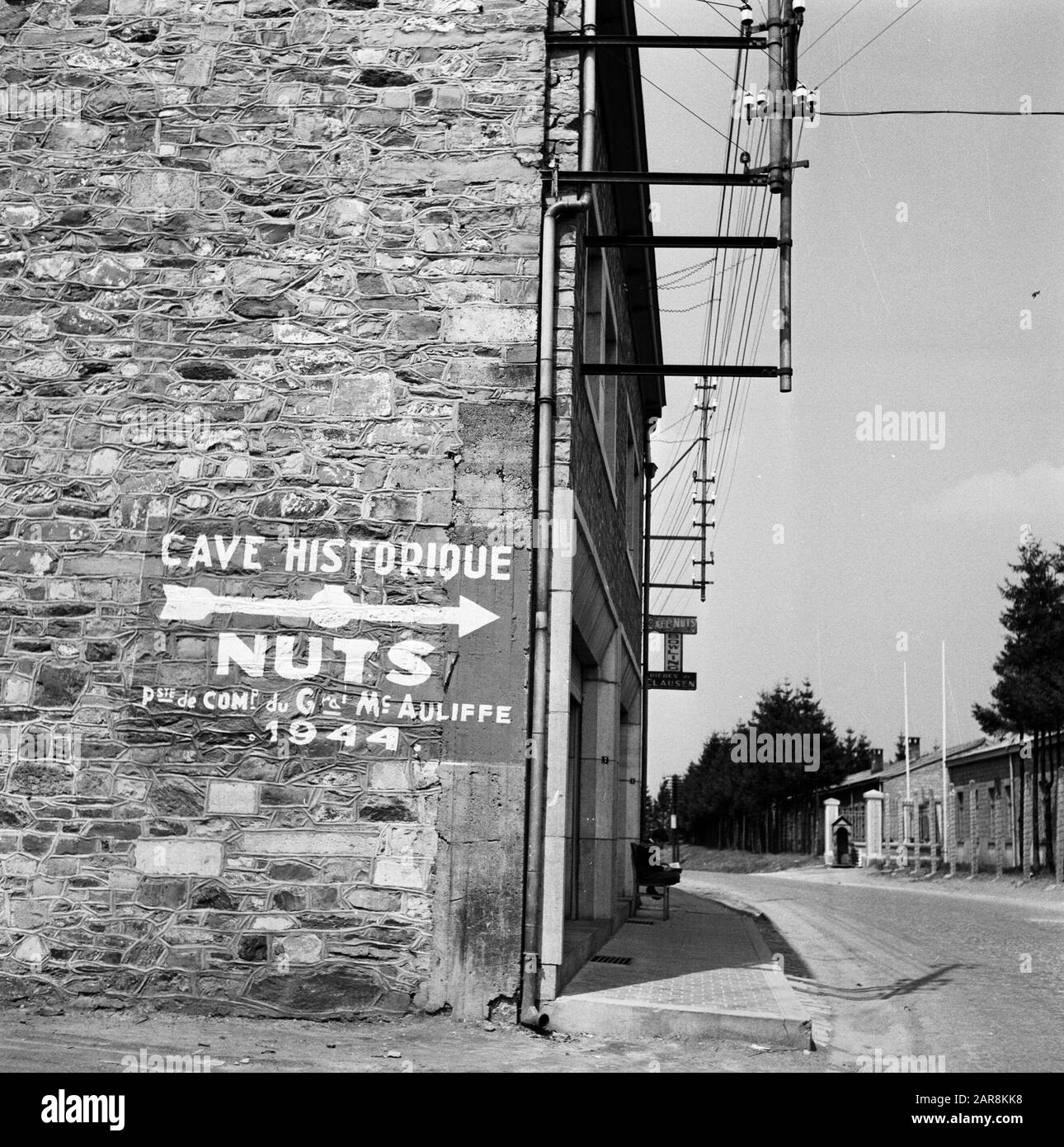 Mémorial du Mardasson, le mémorial de la guerre des États-Unis à Bastogne, Belgique statue de Bastogne; sur le coin de la maison un panneau pointant vers les casernes: Grotte Historique NOIX poste de Comp du gras Mc Auliffe 1944. Annotation : « NUTS (absurdités) se réfère à la réponse donnée par l'unité de thérapie générale américaine McAuliffe à la demande allemande de remise à la bataille de Bastogne en décembre 1944 Date: 1956 lieu: Bastogne, Belgique mots clés: Plaques nominatives, images de rue Banque D'Images