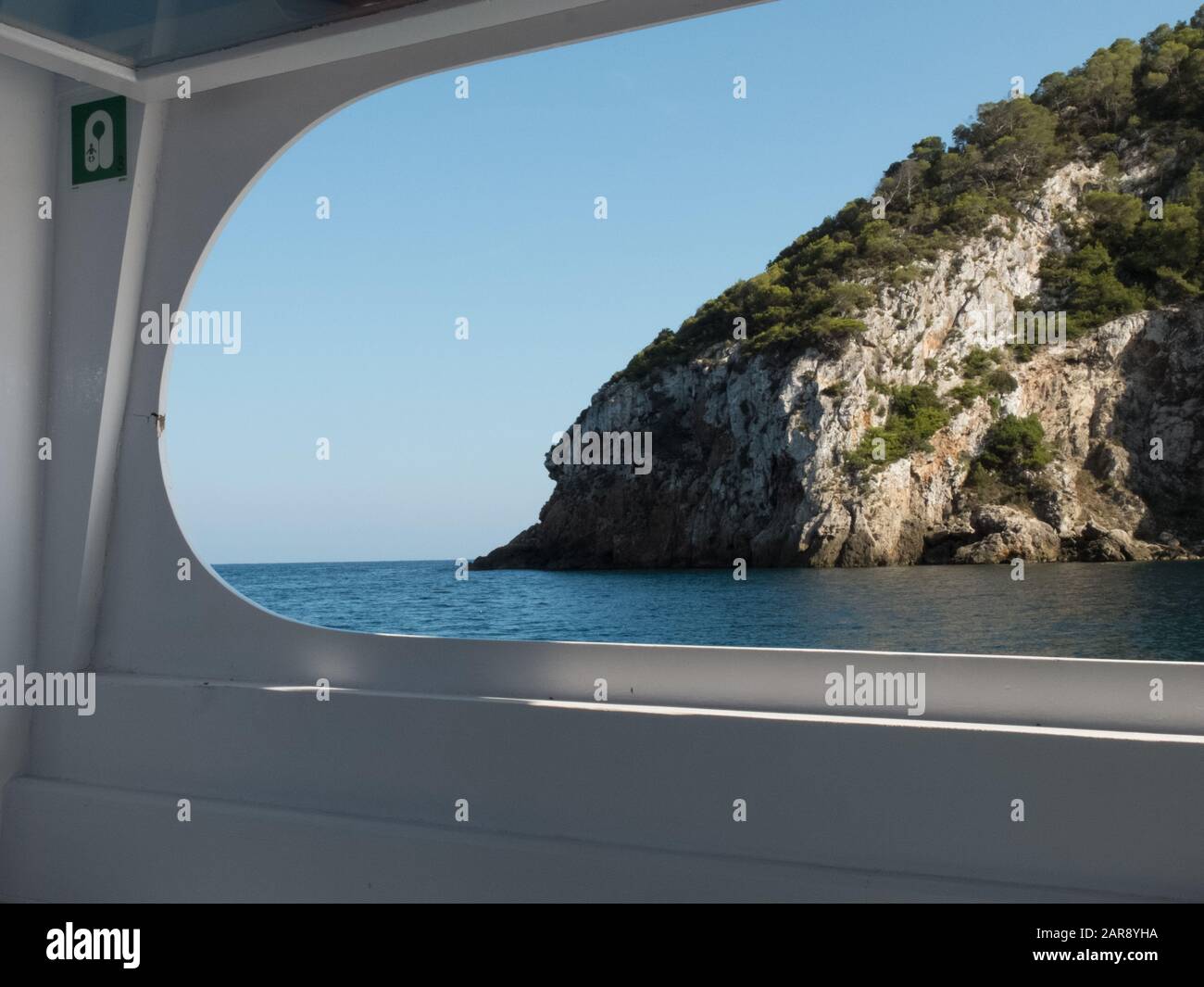 Vue encadrée par la fenêtre d'un bateau-taxi qui quitte la baie de Cala Llonga, Ibiza, les îles Baléares Banque D'Images