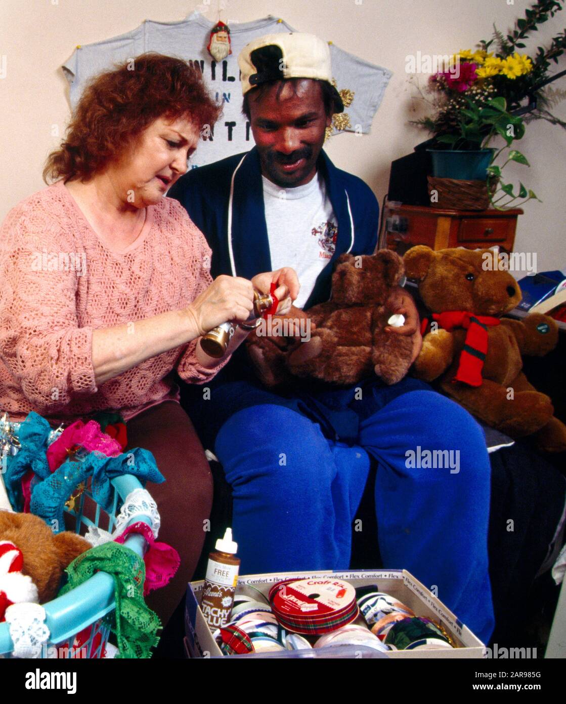 Dans un hospice de Los Angeles, un volontaire applaudit une victime du SIDA mourant en l'aidant à décorer des ours en peluche pour des cadeaux de Noël. Notez le kit de création en premier plan. Banque D'Images