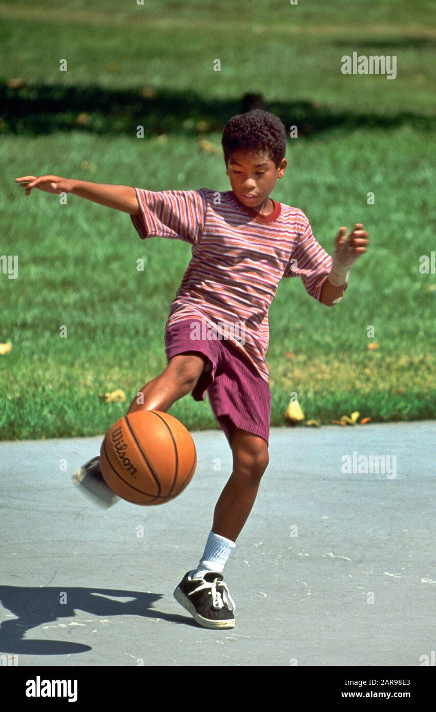 Un garçon de douze ans afro-américain s'équilibre sur un pied alors qu'il attrape un ballon de basket lors d'un match en plein air dans un parc Mission Viejo, CA. Banque D'Images