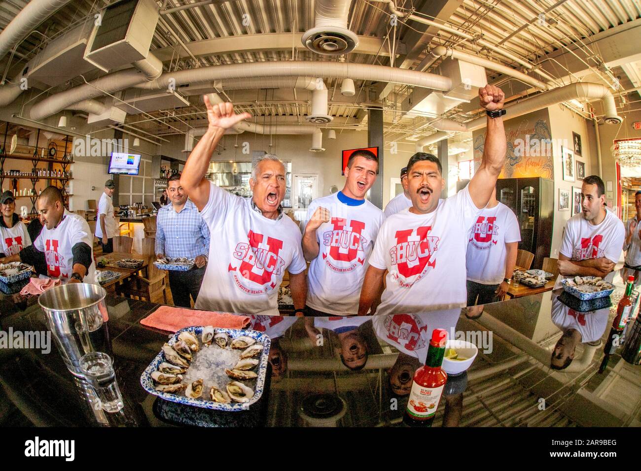 Les participants masculins en T participent à un concours ostréicole dans un restaurant Huntington Beach, Californie. Banque D'Images