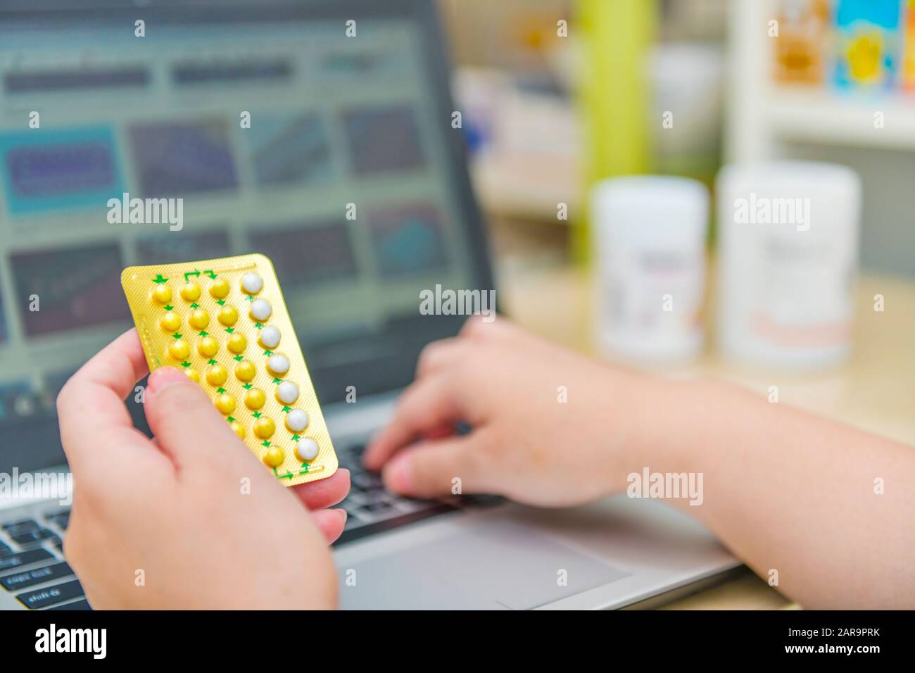 Pharmacien utilisant l'ordinateur portable dans la pharmacie ou la pharmacie. Tenir la main de la boîte de pilules de contrôle de naissance et clé l'ordre de prescription. Banque D'Images