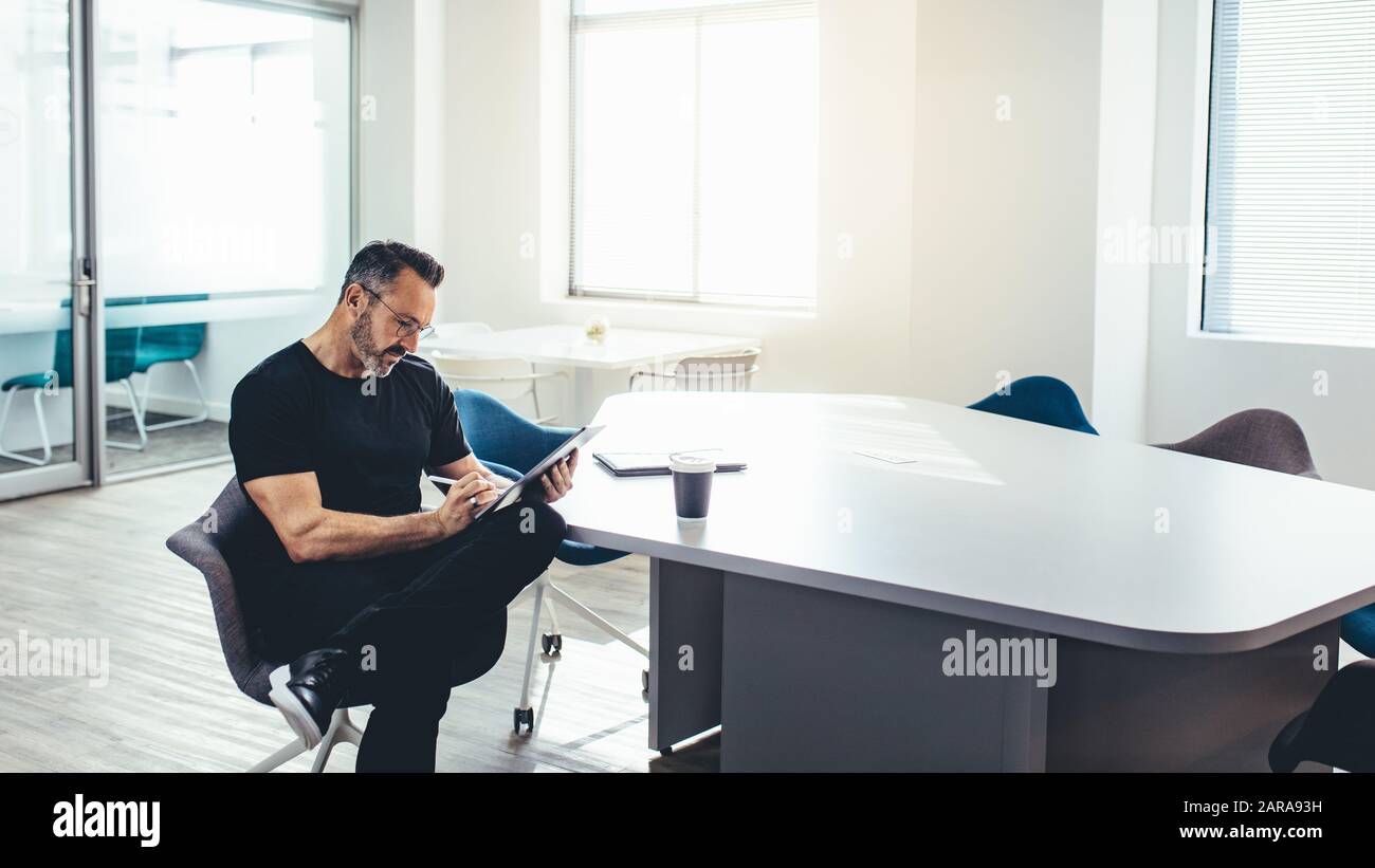Mid adult businessman working on laptop dans un bureau lumineux. Entrepreneur avec sa tablette ordinateur dans un espace de bureau moderne. Banque D'Images