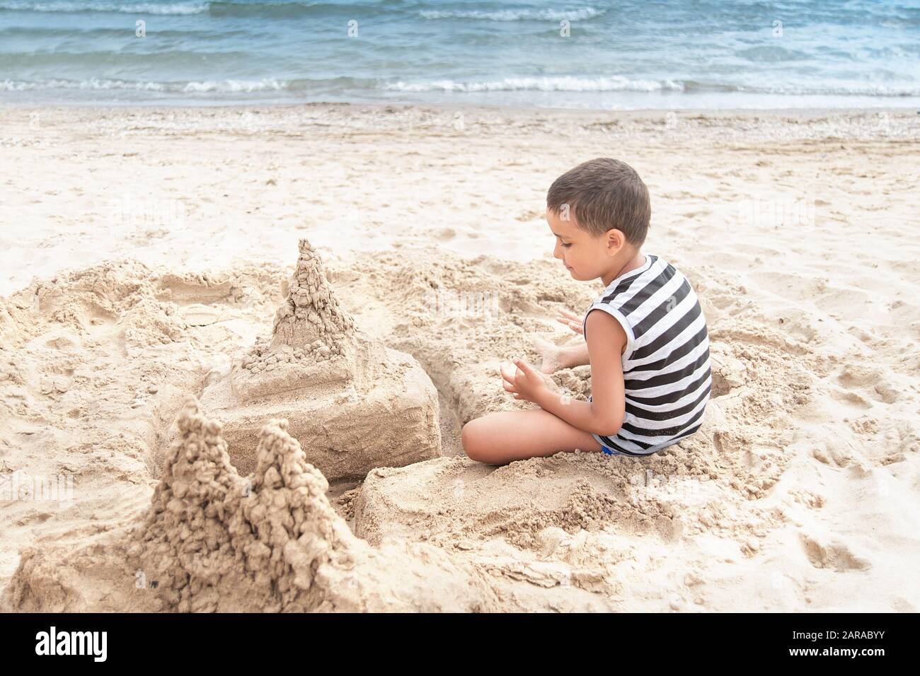 L'enfant construit le château de sable par la mer. Petit enfant sur la  plage jouant avec le sable. Garçon s'amuse en vacances Photo Stock - Alamy