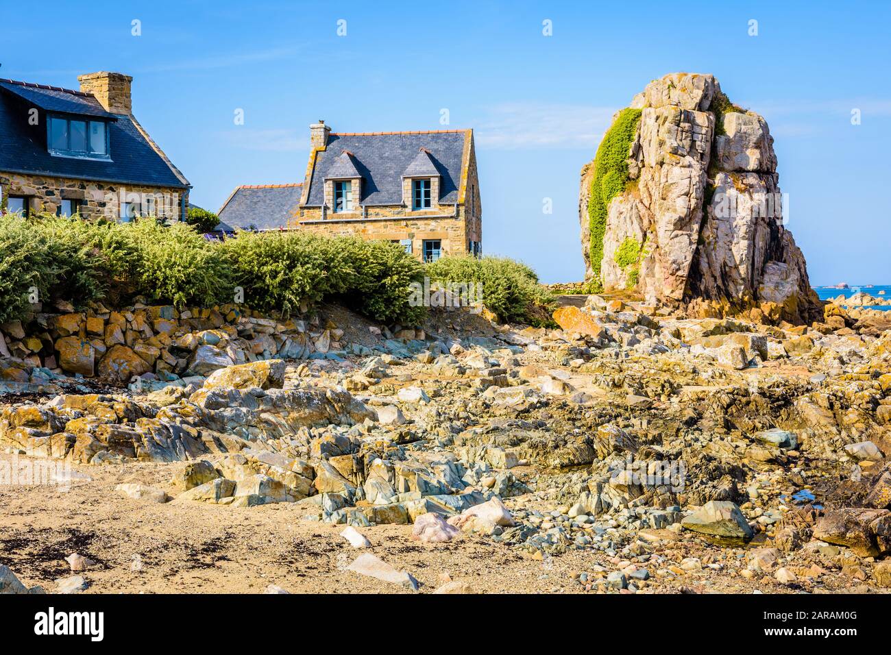 Maisons typiques en granit avec toit en ardoise dans le petit port de Pors Hir en Bretagne, construites sur le bord de mer à côté d'un bloc, par une journée d'été ensoleillée. Banque D'Images
